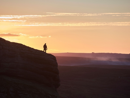 Silhouette of person hiking on large hill at sunset