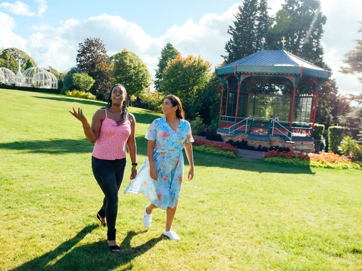 Two women walking on grass past a pergola