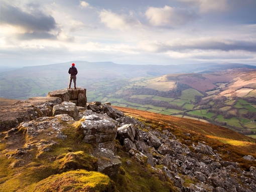 Man atop a vast colourful mountain range at sunset looking out into the valley