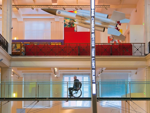 Homme en fauteuil roulant sur une passerelle surélevée dans un musée