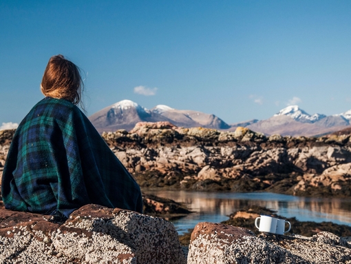 A woman sitting on a rock wrapped in a tartan blanket