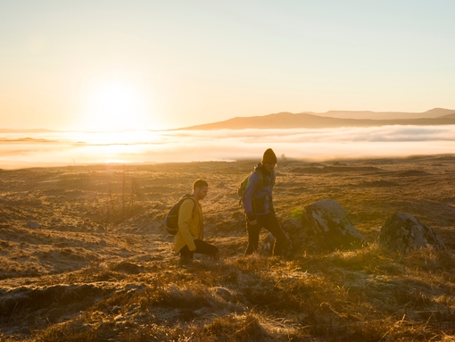 Two men hiking in highlands at sunset. Streaming sunlight