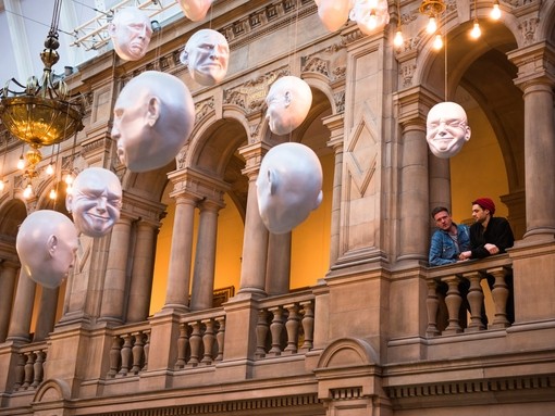Two men looking at installation of suspended head sculptures