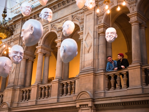 Two men looking at installation of suspended head sculptures