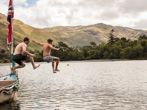 Two men in swimming shorts jumping off a boat into the lake