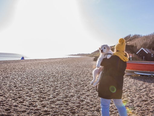 A woman carrying a dog along a beach in Dunwich