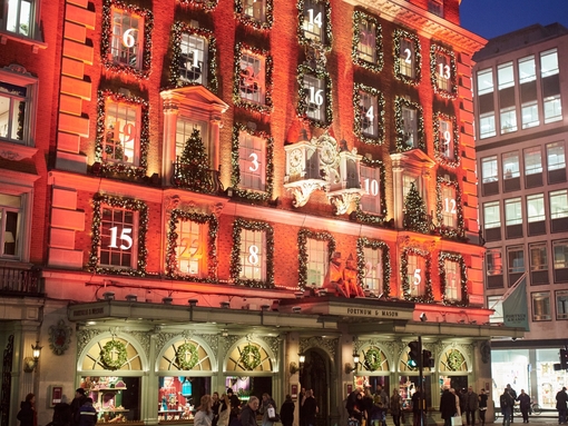 A crowd of people on the street outside Fortnum & Mason in London at night