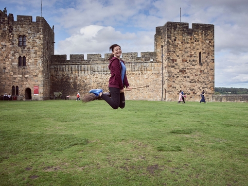 Young woman hovering on a broomstick in the Outer Bailey of Alnwick Castle