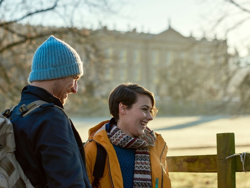 Young couple standing by a wooden fence. Manor in background