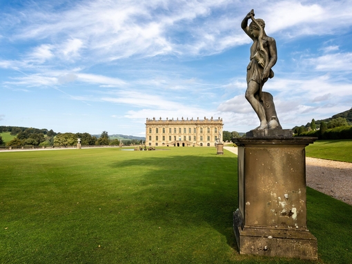 An ornate statue outside a magnificent mansion on flat green lawns