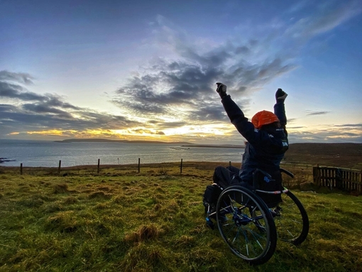 Wheelchair user, arms outstretched, watching the sunrise
