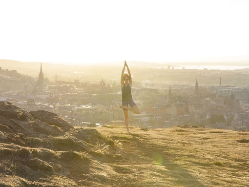An instructor from Adventure Yoga Edinburgh holds a yoga pose on Arthur’s Seat overlooking the city