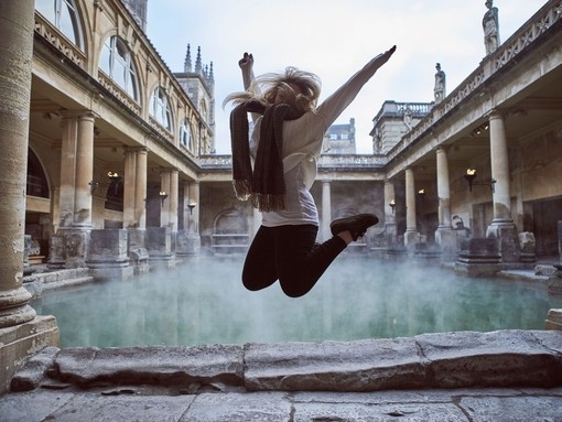 Woman leaping in the air at The Roman Baths, Bath, Somerset, England.