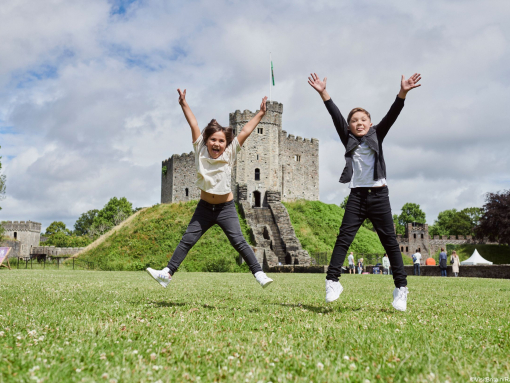 Two children jumping in front of a castle.