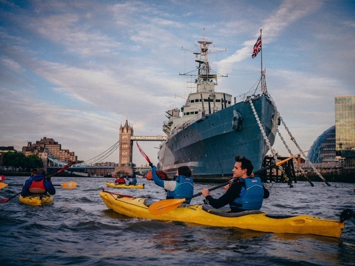 People in Kayaks on river Thames going past HMS Belfast with Tower Bridge in the distance
