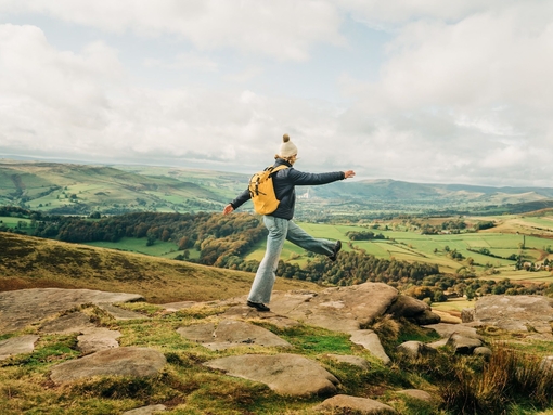 Woman skipping on rocks at edge of hill. Landscape view