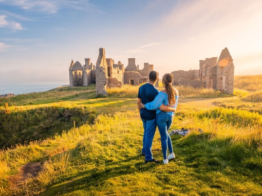 A couple enjoying the views of a castle remains at golden hour.