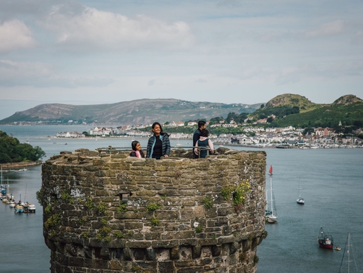Family on top of a castle enjoying river views with boats docked and hills in the distance