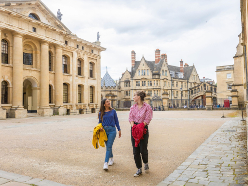 Two women walk across a courtyard among heritage buildings
