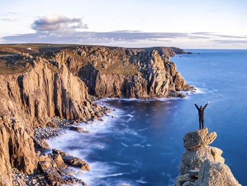 Man standing on a rocky peak on the edge of the coast looking over the headland