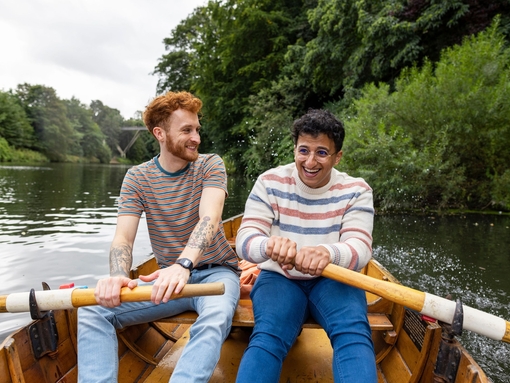 A male couple sitting in a rowboat, rowing together