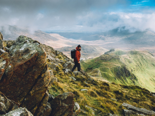 A rugged up man navigating the panoramic summit of a large mountain range