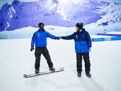 Two men skiing and snowboarding on an indoor snowslope at Chill Factore in Manchester