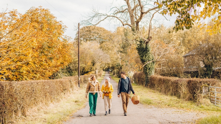 Two women and a man walking on a country lane in autumn