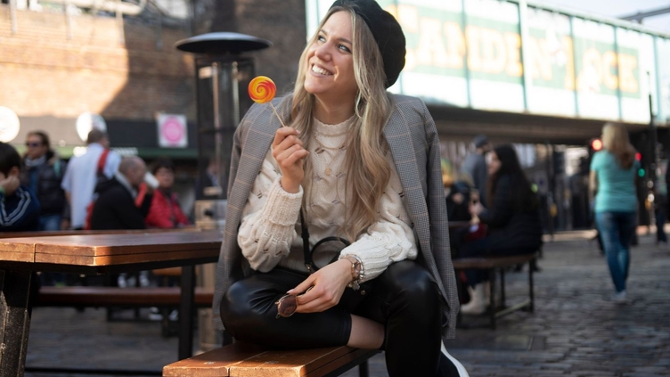 Eine Frau sitzt auf einer Bank, lächelt und hält einen Lutscher