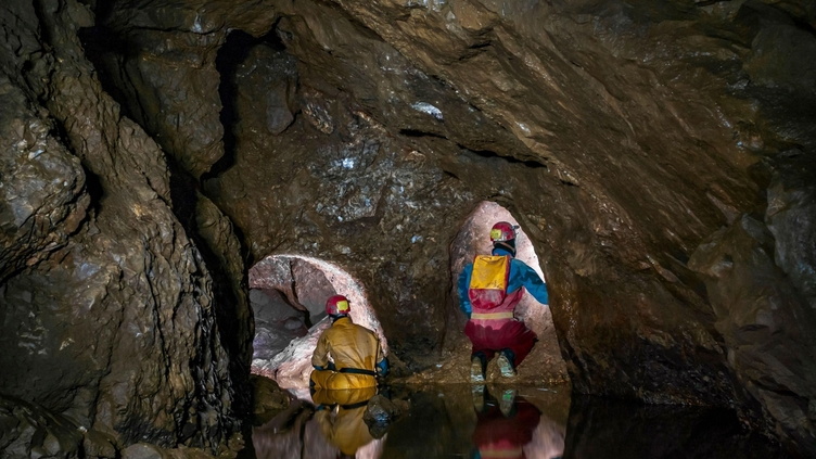 A part-flooded natural cave chamber with two lead miners' tunnels blasted at the far end in Speedwell Cavern in Castleton, Derbyshire.