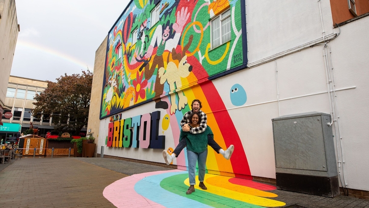 Two people playfully smiling and posing in front of a colourful mural