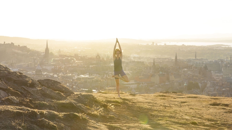 An instructor from Adventure Yoga Edinburgh holds a yoga pose on Arthur’s Seat overlooking the city