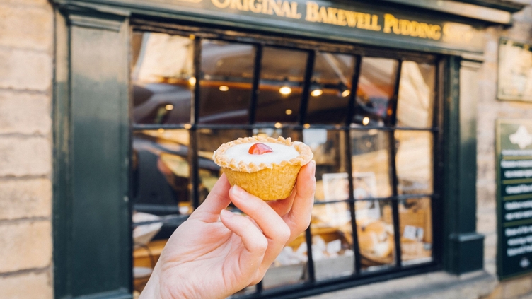 Hand holding Bakewell tart in front of bakery
