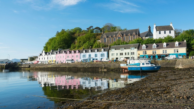 Pastel-coloured houses line the stony harbour at Portree on a sunny day.