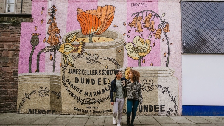 A man and a woman hugging in front of the marmalade mural.