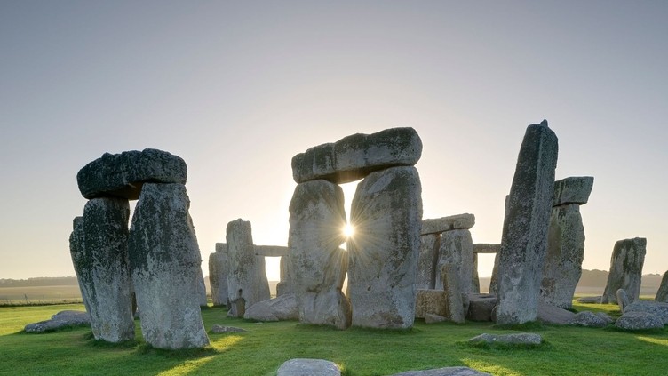 Large stone pillars arranged in circle on grass. Sunset