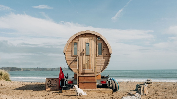 A purpose built beach sauna parked on the sand by the ocean's edge.