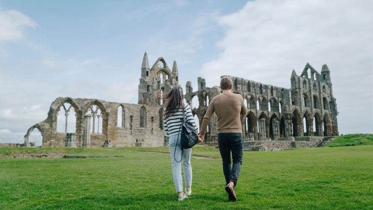 A man and woman walking towards a heritage Abbey building