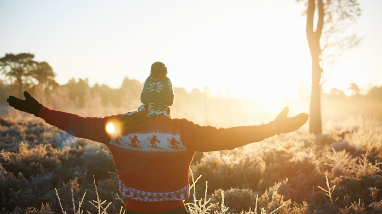 Man with arms outstretched wearing hat and gloves in the winter sun