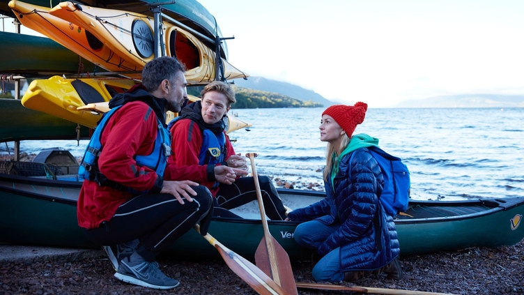 Un groupe de personnes sur le rivage, avec une pile de kayaks