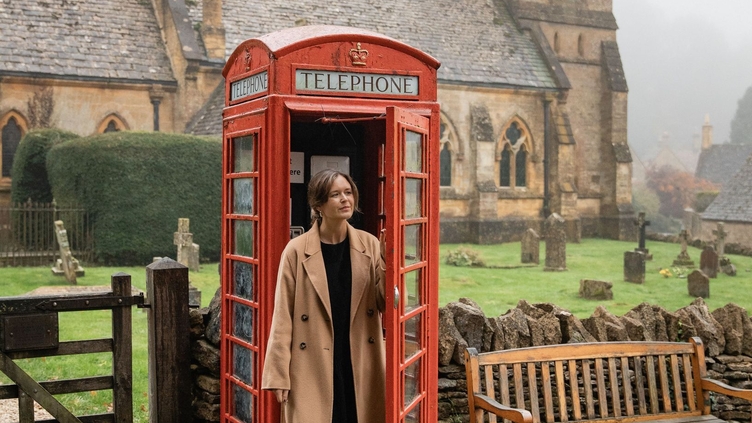 A woman exits a red telephone box with a church in the background