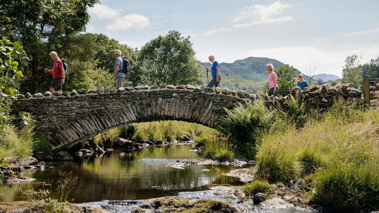 Group of friends out walking in the lakes crossing bridge in the Lake District