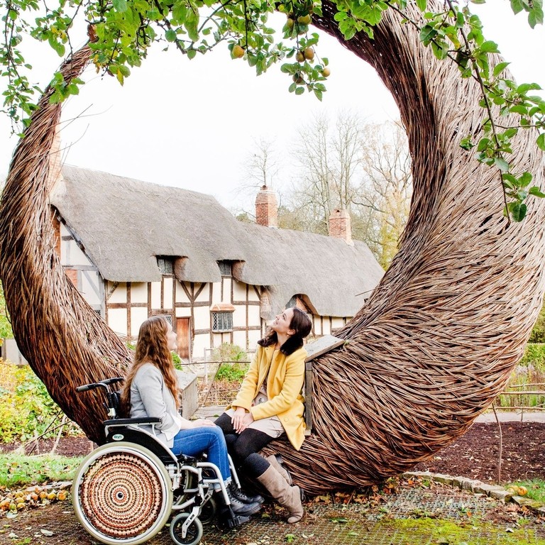 Two women at Anne Hathaway's Cottage sitting on Tom Hare's 'The Moon Seat', Stratford-upon-Avon, Warwickshire, England