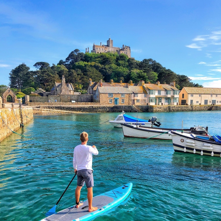 A man paddleboarding in a harbour in clear turquoise waters with a tidal island in the background.
