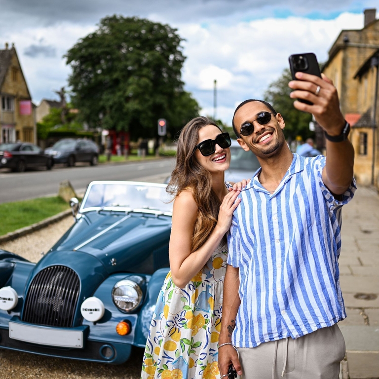 A man and a woman take a selfie in front of a classic car